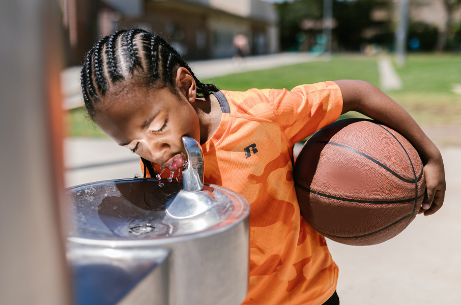 Child holding basketball drinks from water fountain
