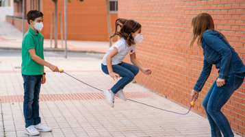 Kids playing jump rope wearing masks.