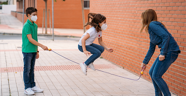Kids playing jump rope wearing masks.