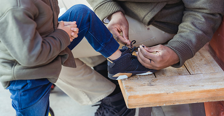 An adult fixes a child's shoelaces.